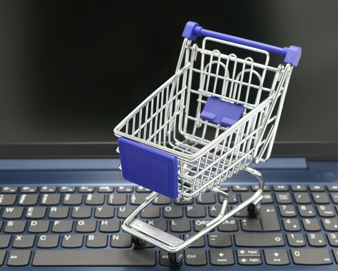 vision A mini shopping cart placed on a laptop keyboard, symbolizing online shopping and digital retail.
