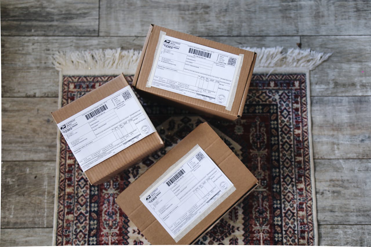 about-img Three labeled delivery boxes placed on a decorative rug over a wooden floor.