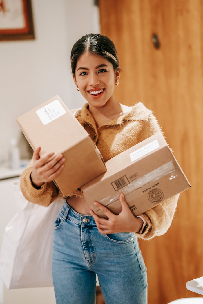 services-img Smiling young ethnic lady in casual outfit standing in light room in house with packages and shopping bag while looking at camera